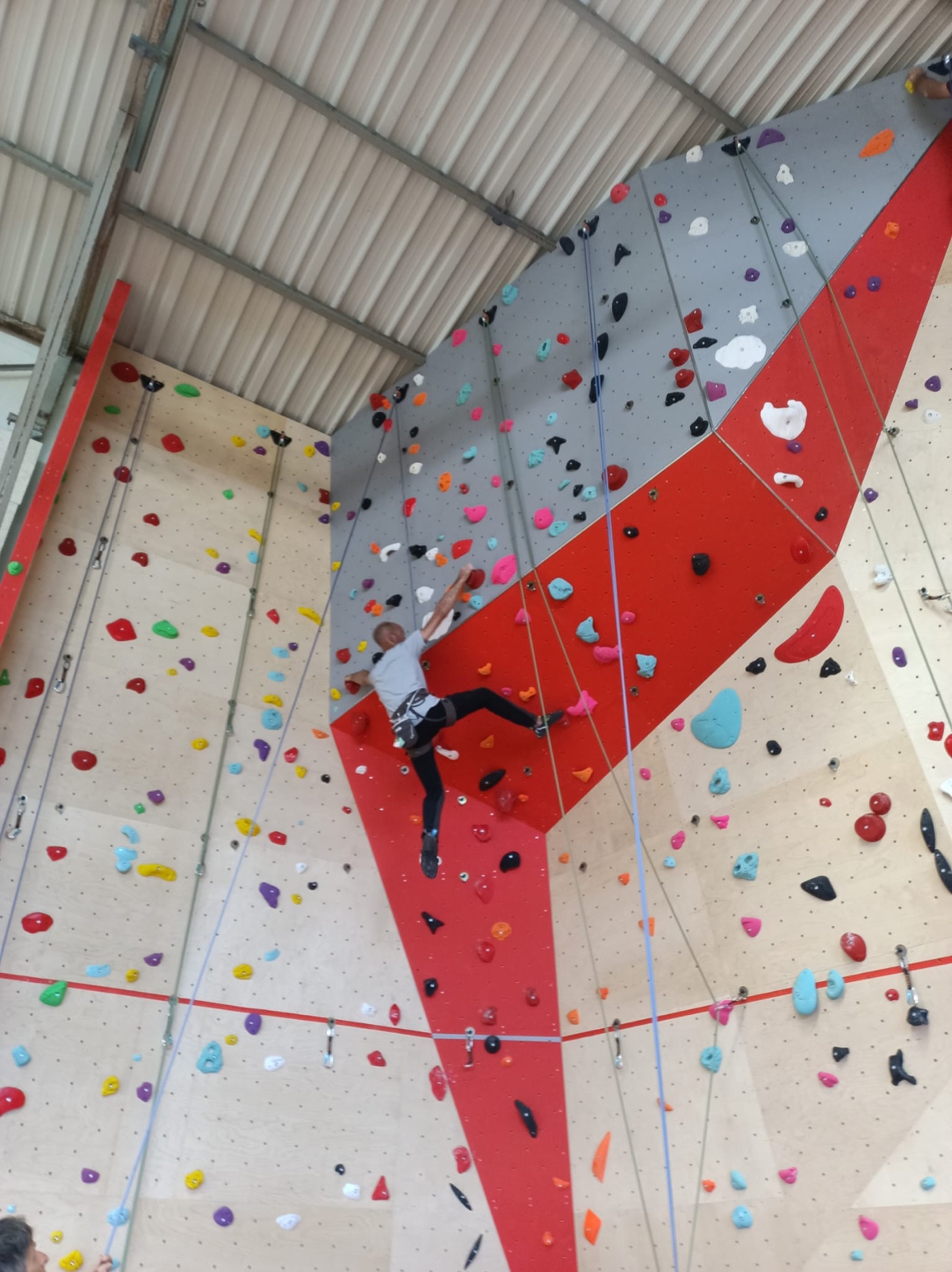 Un grimpeur progresse sur le grand mur rouge et gris